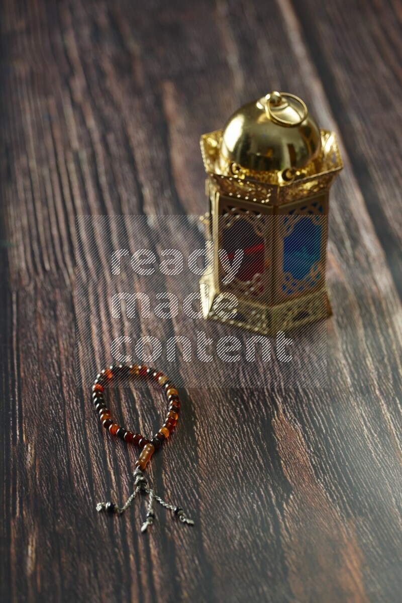 A golden lantern with different drinks, dates, nuts, prayer beads and quran on brown wooden background