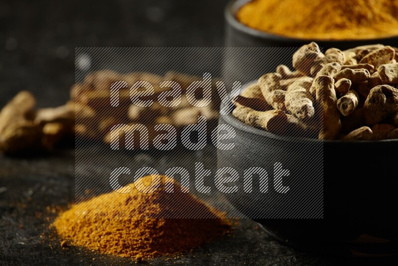 وعاءان من الفخار باللون الأسود، أحدهما ممتلئ ببودرة الكركم والآخر ممتلئ بأصابع كاملة من الكركم المجفف على خلفية سوداء