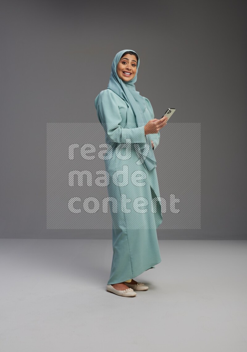 Saudi Woman wearing Abaya standing texting on phone on Gray background