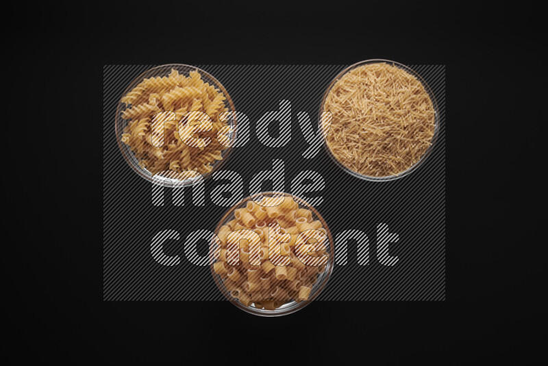 Different pasta types in glass bowls on black background