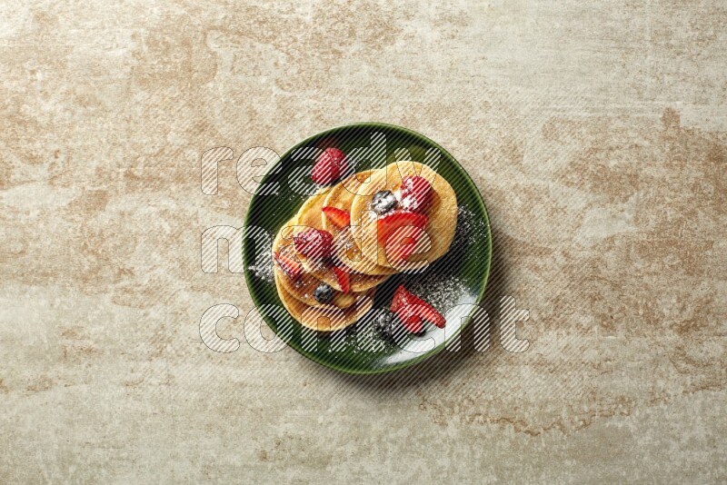 Five stacked mixed berries mini pancakes in a green plate on beige background