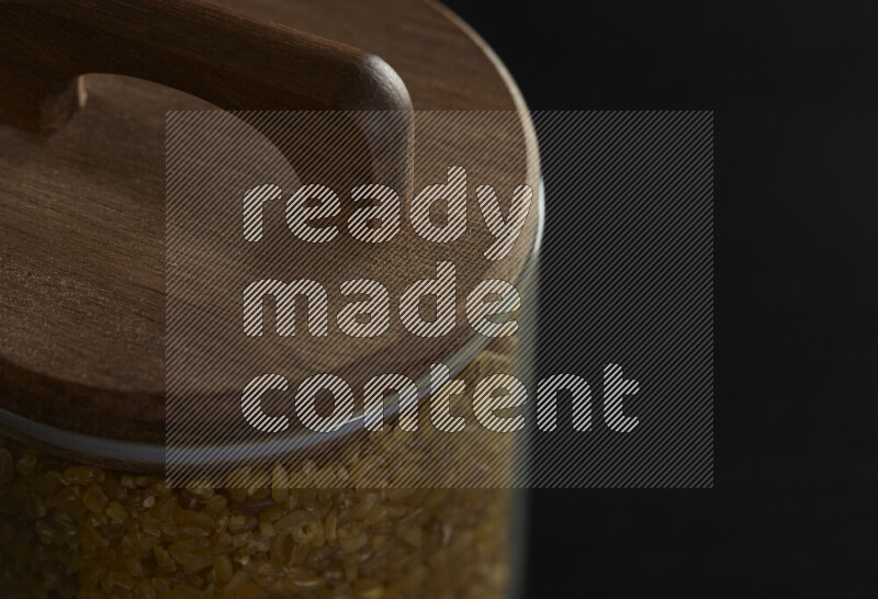 Coarse bulgur in a glass jar on black background
