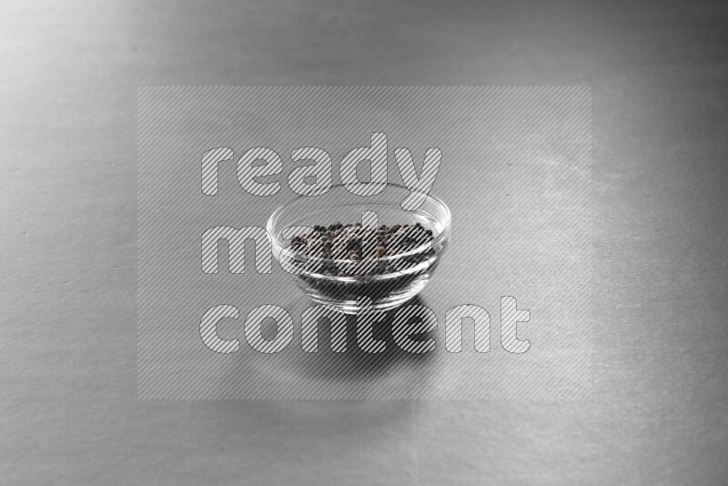 A glass bowl full of black peppers on black flooring