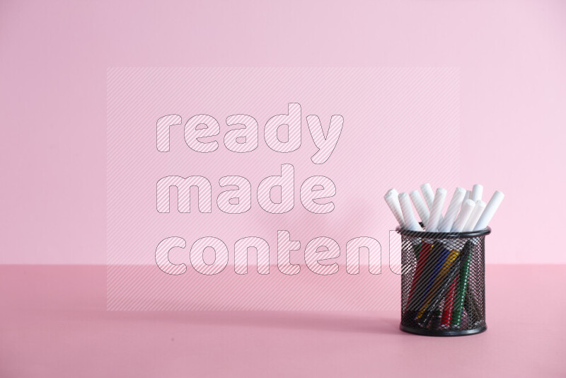 Pens, pencils and other different school supplies in a metal pen holder on rose background