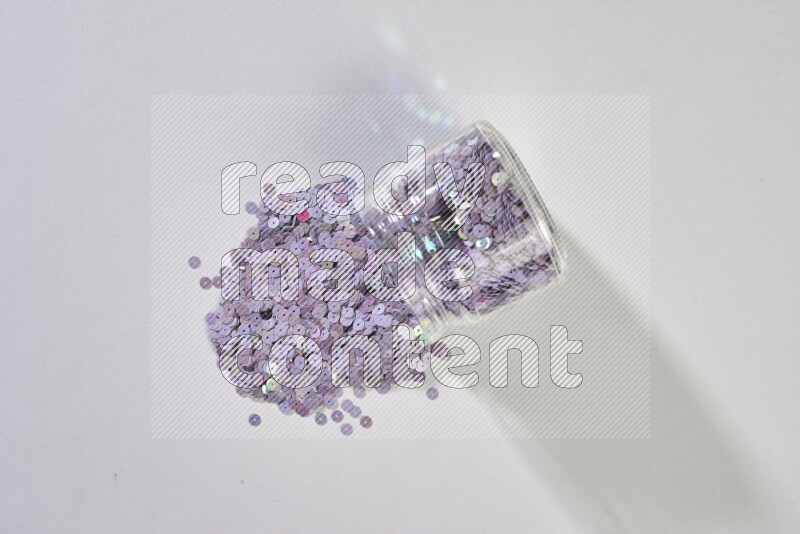 Colored flat sequins in a glass jar on grey background
