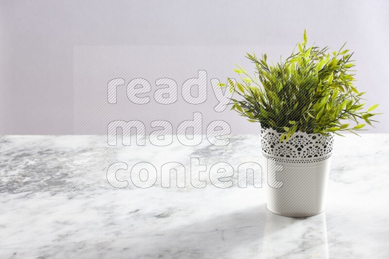 Green artificial plant in white decorative pot on grey marble background