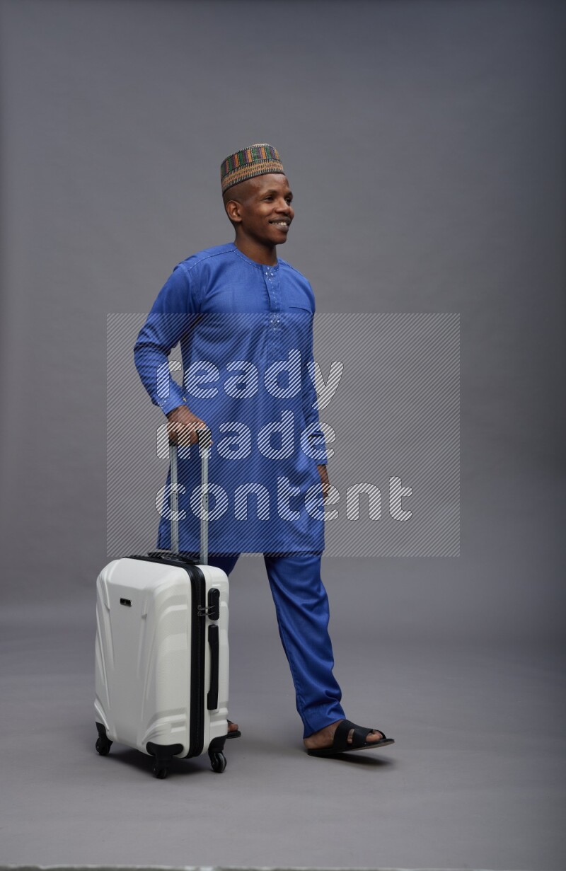 Man wearing Nigerian outfit standing holding bag on gray background