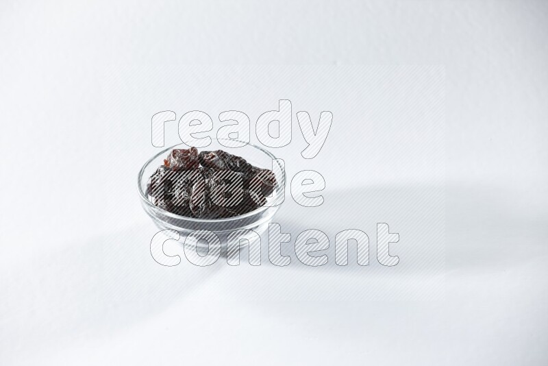 A glass bowl full of dried plums on a white background in different angles
