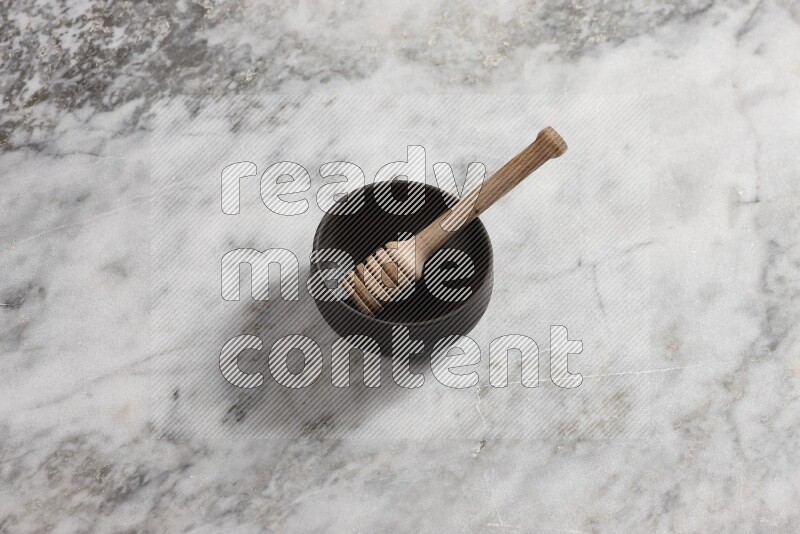 Black pottery bowl with wooden honey dipper in it on grey marble background