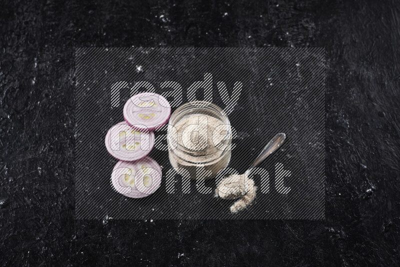 A glass jar full of onion powder on black background