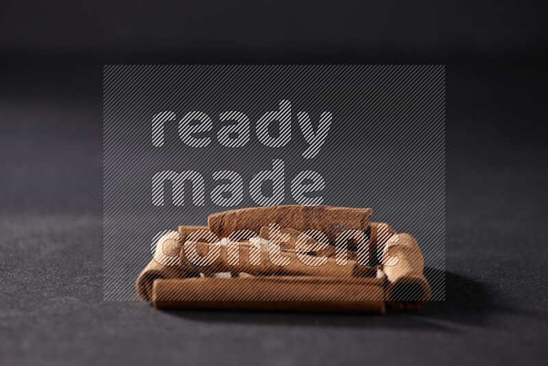 أربعة من أعواد القرفة مكونة شكل مربع بداخلها أعواد قرفة صغيرة علي خلفية سوداء