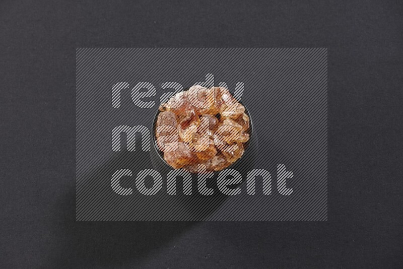 A black pottery bowl full of gum arabic on black flooring