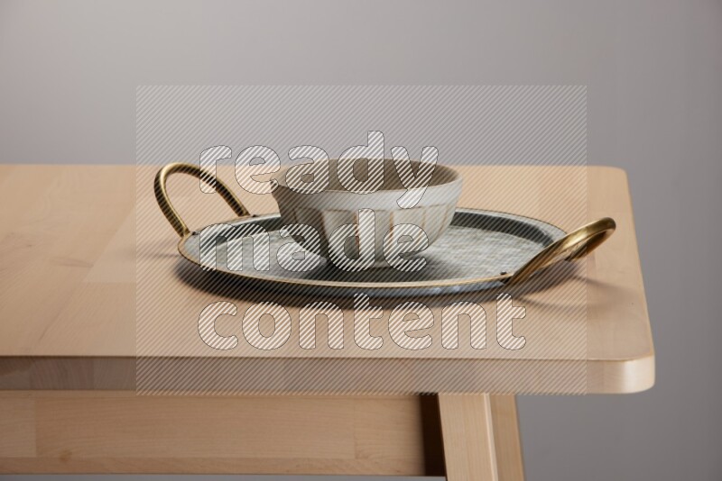 off white bowl placed on a rounded stainless steel tray with golden handels on the edge of wooden table