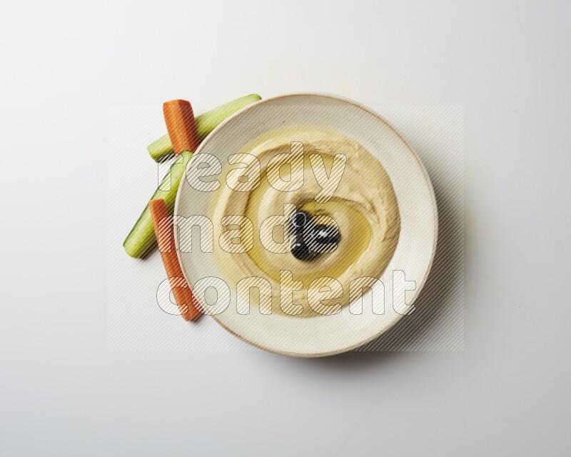 Hummus in a pottry plate garnished with black olives on a white background