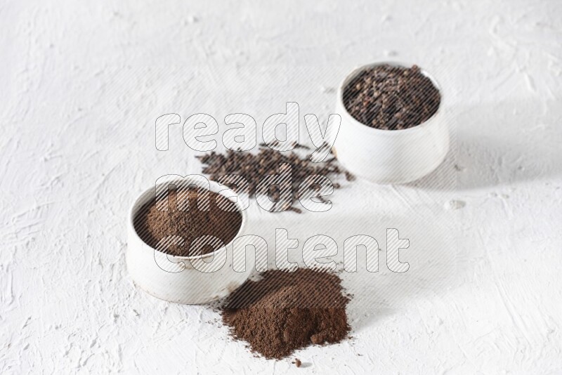 2 Beige ceramic bowls, one full of cloves and the other full of powder on textured white flooring