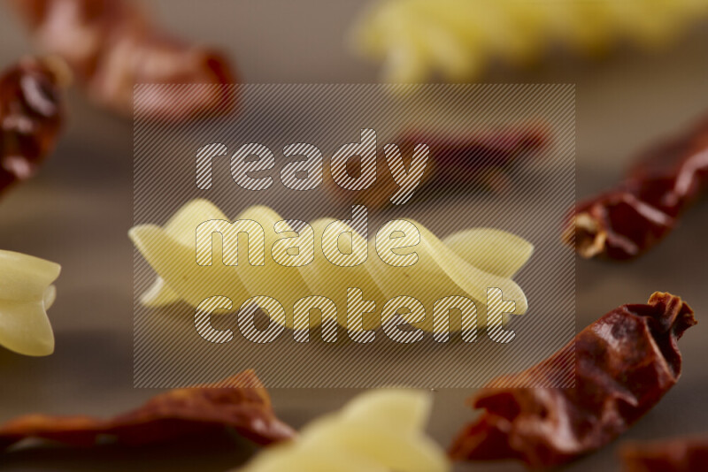 Raw pasta with different ingredients such as cherry tomatoes, garlic, onions, red chilis, black pepper, white pepper, bay laurel leaves, rosemary and cardamom on beige background