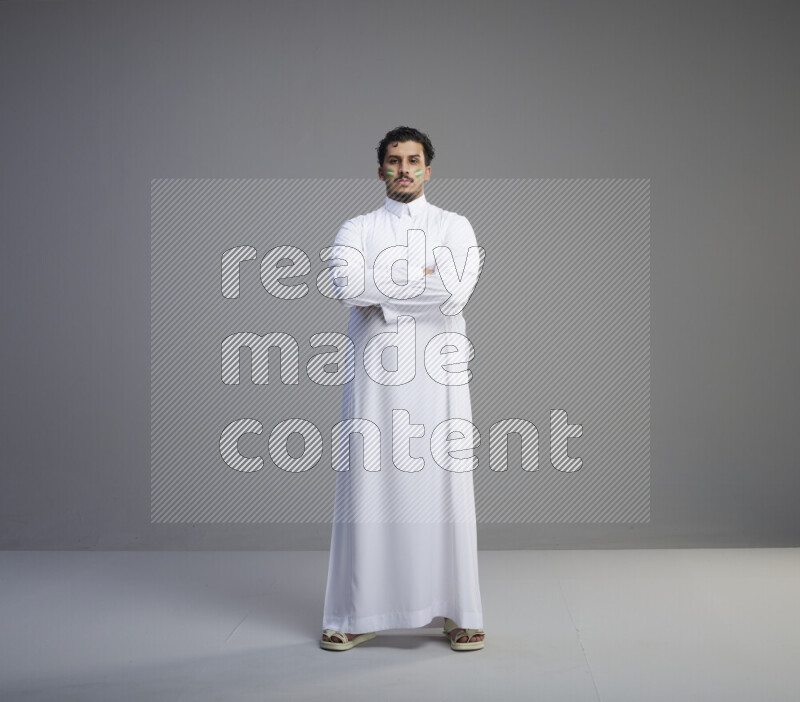 A Saudi man standing wearing thob with face painting interacting with the camera on gray background