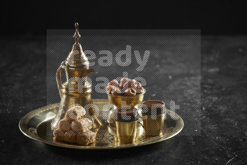 Oriental sweets with dates and a drink on a metal tray in a dark setup
