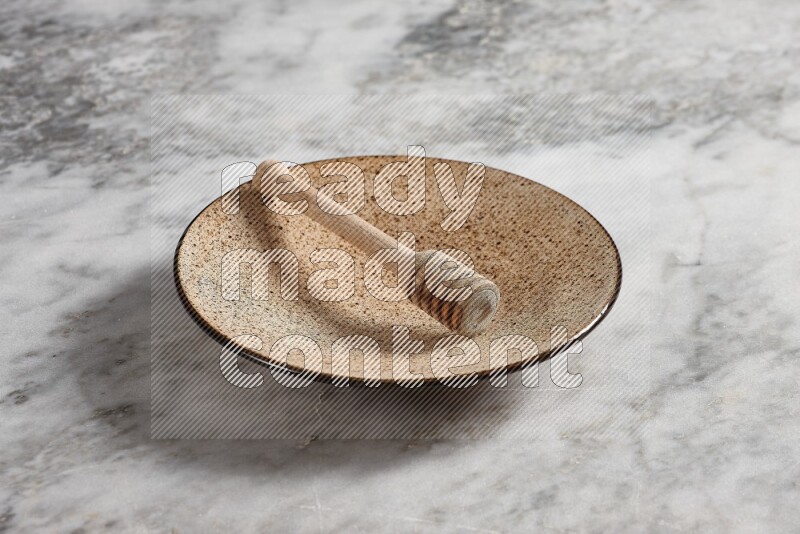 Multicolored pottery plate with wooden honey dipper in it on grey marble background