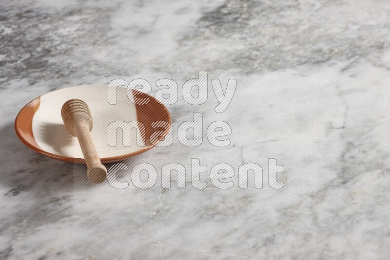 Multicolored pottery plate with wooden honey dipper in it on grey marble background