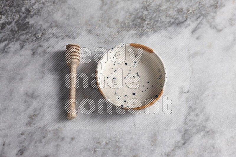 Multicolored pottery bowl with wooden honey dipper on the side on grey marble background