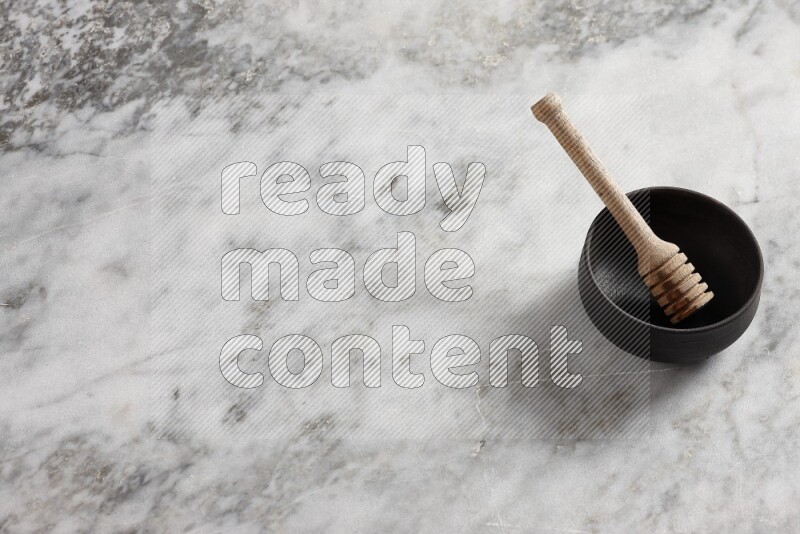 Black pottery bowl with wooden honey dipper in it on grey marble background