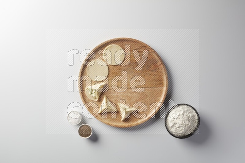 two closed sambosas and one open sambosa filled with cheese while flour, salt, and black pepper aside in a wooden dish on a white background