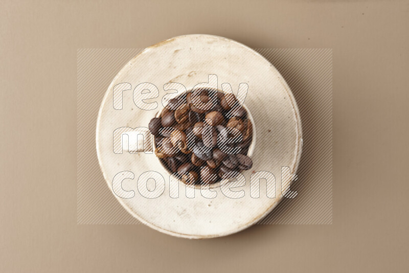 A beige pottery cup full of roasted coffee beans on beige background