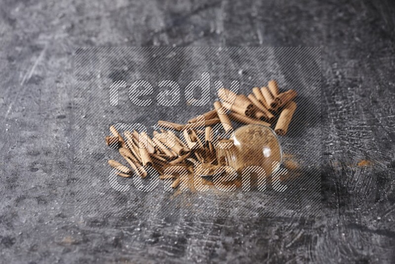 Herbal glass jar full cinnamon powder flipped and a metal spoon full of powder surrounded by cinnamon sticks on textured black background in different angles