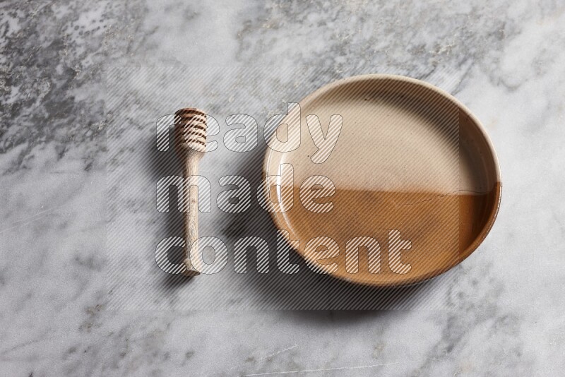 Multicolored pottery oven plate with wooden honey dipper on the side on grey marble background