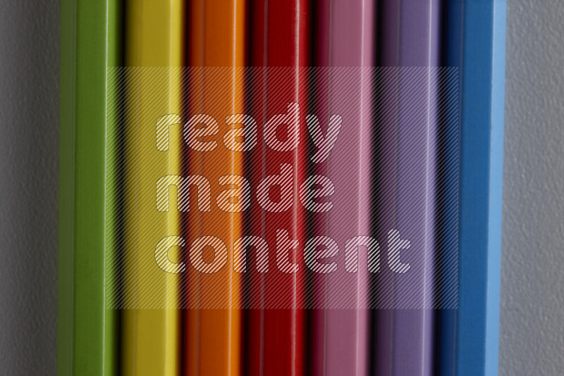 A collection of colored pencils arranged showcasing a gradient of different hues on grey background