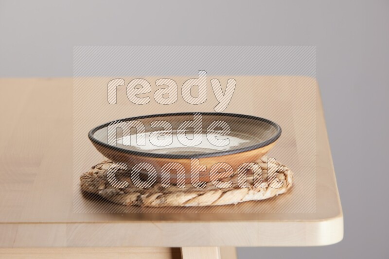 multi-colored pottery Plate placed on a small light colored straw placemat on the edge of wooden table