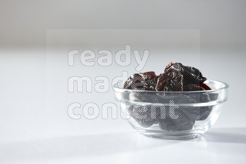 A glass bowl full of dried plums on a white background in different angles