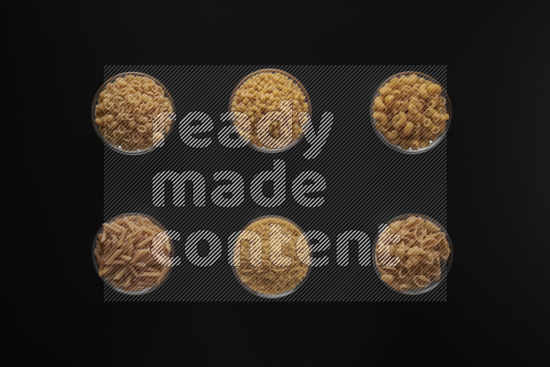 Different pasta types in 6 glass bowls on black background