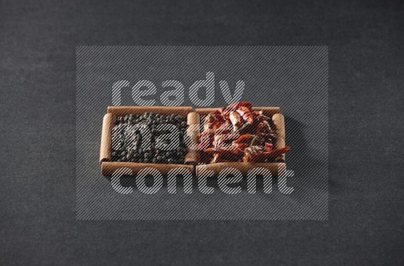 مربعان من أعواد القرفة ممتلئان بالفلفل الحار المجفف وحبوب الفلفل الأسود علي خلفية سوداء