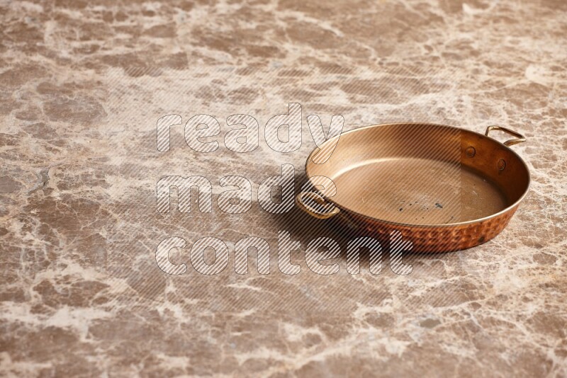 A small copper pan on beige marble background