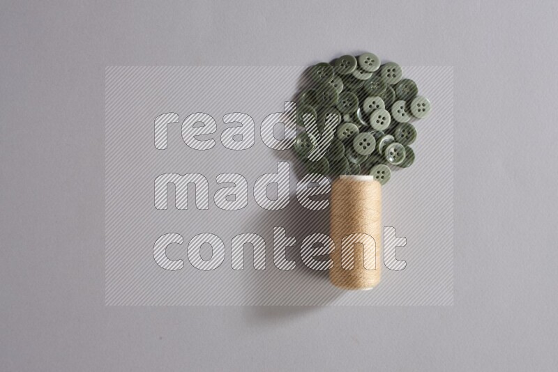 A beige sewing thread spool with colored buttons on grey background