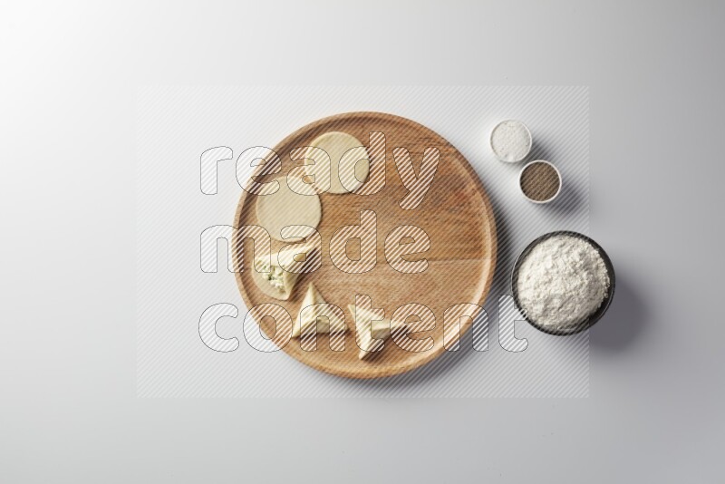 two closed sambosas and one open sambosa filled with cheese while flour, salt, and black pepper aside in a wooden dish on a white background