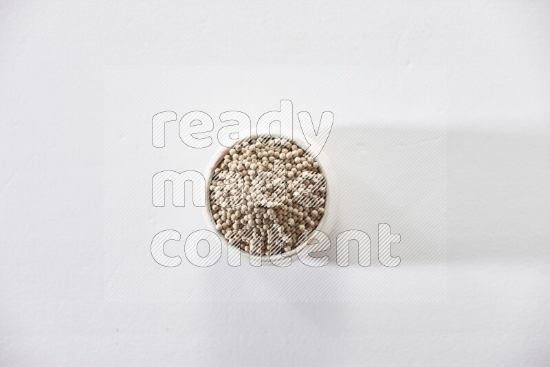 A beige pottery bowl full of white pepper beads on white flooring