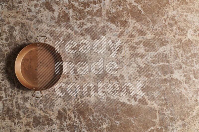 A small copper pan on beige marble background