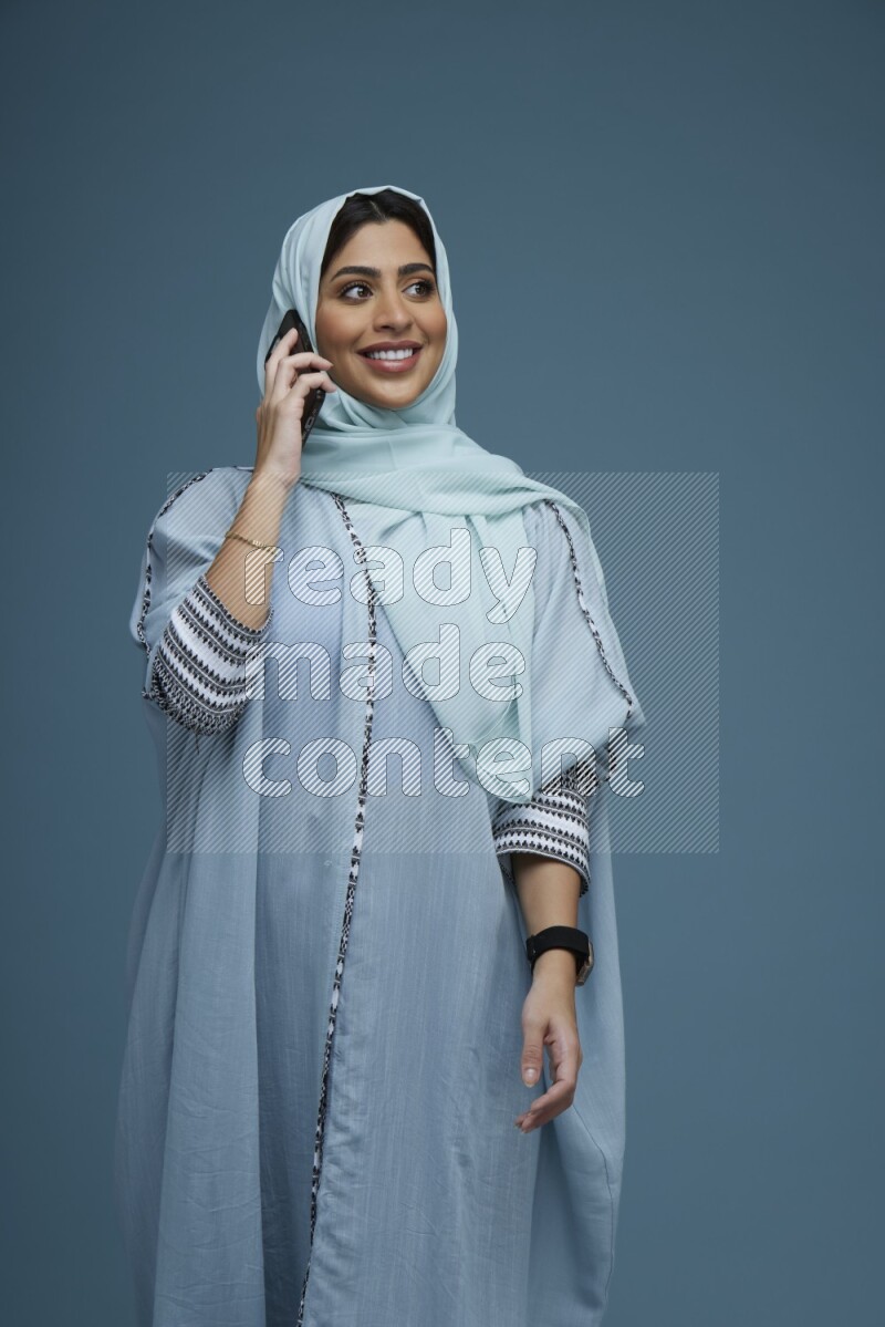 A Saudi woman having a Call in a blue background wearing blue Abaya with hijab