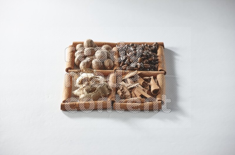 4 مربعات من أعواد القرفة ممتلئة بحبوب القهوة وجوزة الطيب والقرفة والزنجبيل المجفف على أرضية بيضاء