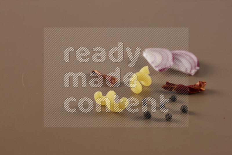 Raw pasta with different ingredients such as cherry tomatoes, garlic, onions, red chilis, black pepper, white pepper, bay laurel leaves, rosemary and cardamom on beige background