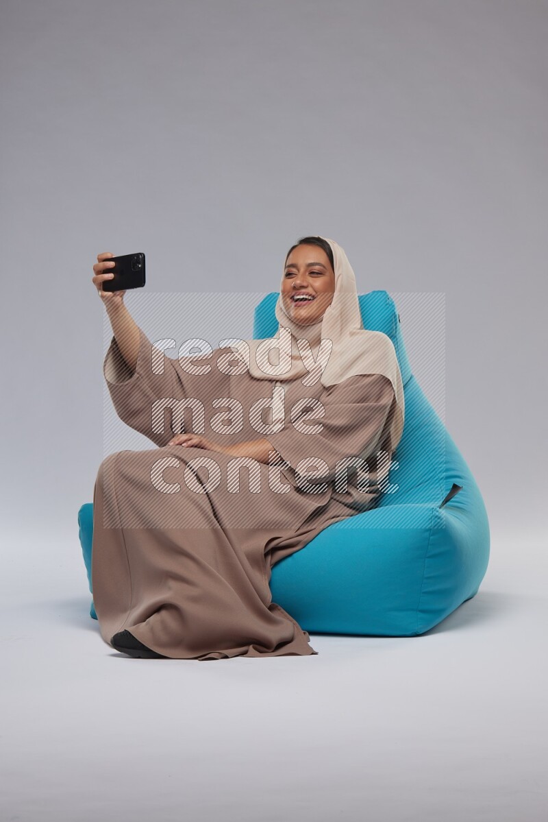 A Saudi woman sitting on a blue beanbag and taking selfie