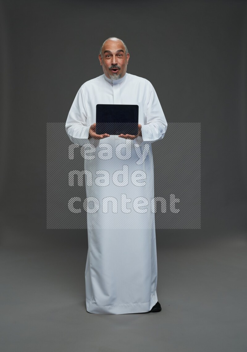 Saudi man without shomag Standing working on tablet on gray background