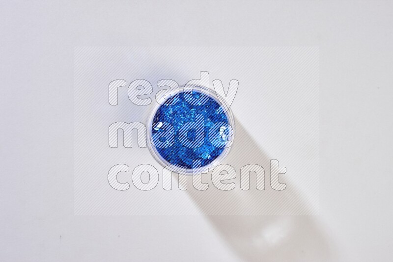 Colored flat sequins in a glass jar on grey background
