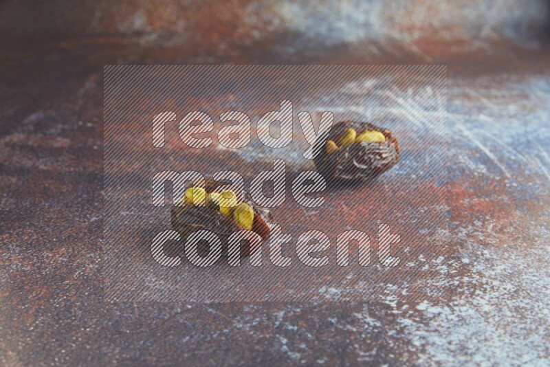 two pistachio stuffed madjoul dates on a rustic reddish background