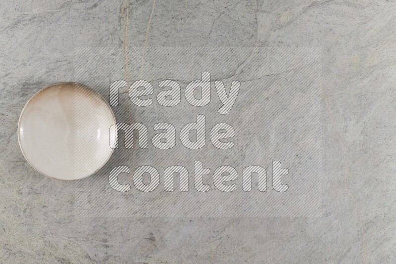 A circular beige pottery plate on grey marble background