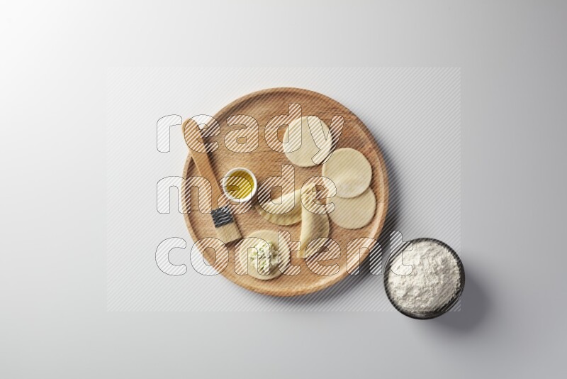 two closed sambosas and one open sambosa filled with cheese while flour, and oil with oil brush aside in a wooden dish on a white background