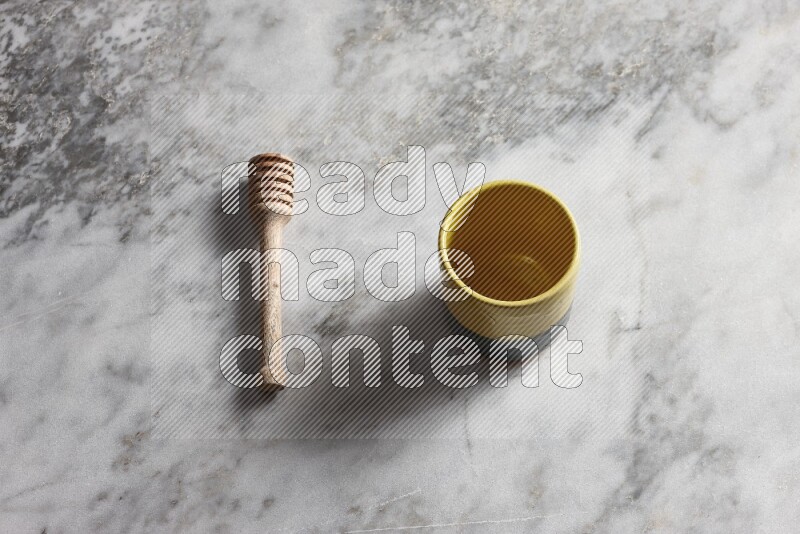 Multicolored pottery cup with wooden honey dipper on the side on grey marble background